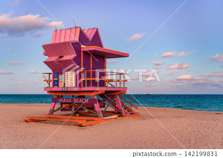 Lifeguard tower on the sandy Miami Beach shore. Iconic Art Deco lifeguard station under summer sky. Scenic view of South Beach coastline in Florida. Colorful lifeguard tower, symbol of Miami tourism. Lifeguard tower on the sandy Miami Beach shore. Iconic Art Deco lifeguard station under summer sky. Scenic view of South Beach coastline in Florida. Colorful lifeguard tower, symbol of Miami tourism. 142199831