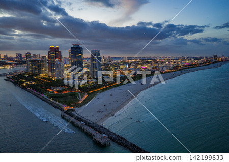 Aerial night view of Miami coastline. Twilight skyline above the Miami oceanfront. Miami Beach waterfront with dramatic sky. Aerial night view of Miami coastline. Twilight skyline above the Miami oceanfront. Miami Beach waterfront with dramatic sky. 142199833