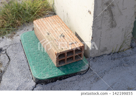 Orange brick on green utility cover in cracked asphalt ground Orange brick on green utility cover in cracked asphalt ground 142199855