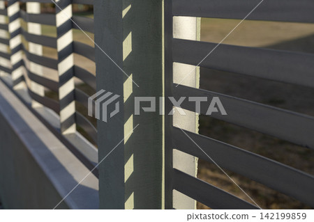 Grey metal fence with horizontal slats and shadows 142199859
