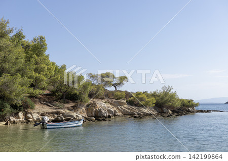 Small blue boat anchored on rocky coastline with green trees Small blue boat anchored on rocky coastline with green trees 142199864