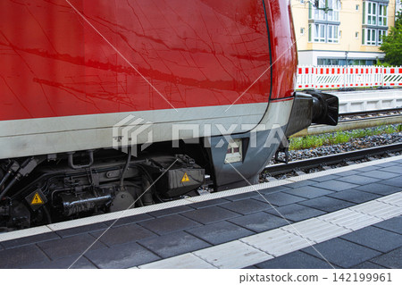 Closeup view of a red train at a modern urban platform with tactile safety tiles and rail tracks. Closeup view of a red train at a modern urban platform with tactile safety tiles and rail tracks. 142199961