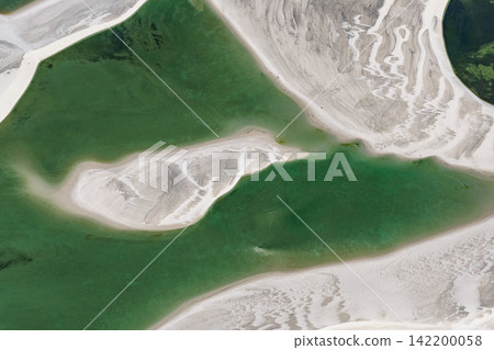 An aerial view from directly above Lençóis Maranhenses, showing a green lagoon bordering white sand formations. An aerial view from directly above Lençóis Maranhenses, showing a green lagoon bordering white sand formations. 142200058