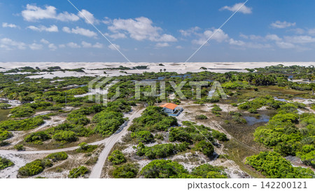 An aerial view of a hut nestled in a shrubbery marsh and white sand dunes, Lençóis Maranhenses. An aerial view of a hut nestled in a shrubbery marsh and white sand dunes, Lençóis Maranhenses. 142200121