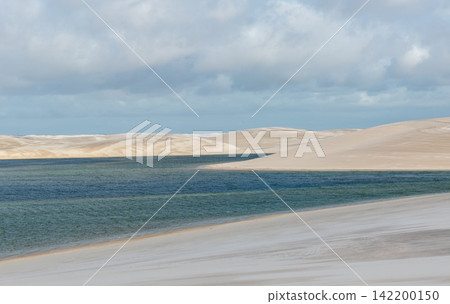 Under a cloudy sky, the blue-green lagoon of Lençóis Maranhenses stretches along the white sand dunes. Under a cloudy sky, the blue-green lagoon of Lençóis Maranhenses stretches along the white sand dunes. 142200150