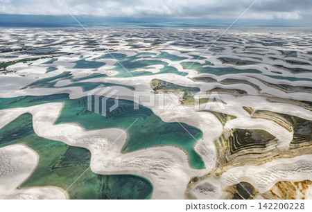 Aerial view of white sand dunes and a blue-green lagoon stretching to the horizon of storm clouds, Lençóis Maranhenses. Aerial view of white sand dunes and a blue-green lagoon stretching to the horizon of storm clouds, Lençóis Maranhenses. 142200228