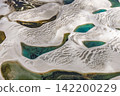 An aerial view from directly above Lençóis Maranhenses, a blue-green lagoon surrounded by patterns of white sand dunes. 142200229