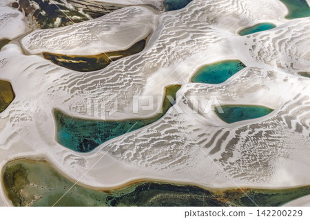 An aerial view from directly above Lençóis Maranhenses, a blue-green lagoon surrounded by patterns of white sand dunes. An aerial view from directly above Lençóis Maranhenses, a blue-green lagoon surrounded by patterns of white sand dunes. 142200229