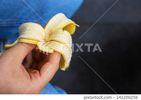 Closeup of a hand holding a banana peel against a soft blue denim background. Closeup of a hand holding a banana peel against a soft blue denim background. 142200256