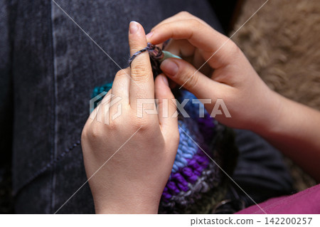 Closeup photo of young womans hands crocheting a colorful scarf using a crochet hook and vibrant yarn. Closeup photo of young womans hands crocheting a colorful scarf using a crochet hook and vibrant yarn. 142200257