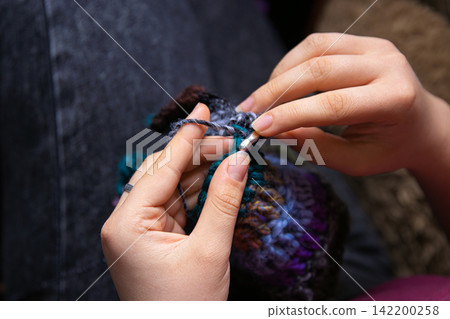 Closeup photo of young womans hands crocheting a colorful scarf using a crochet hook and vibrant yarn. Closeup photo of young womans hands crocheting a colorful scarf using a crochet hook and vibrant yarn. 142200258