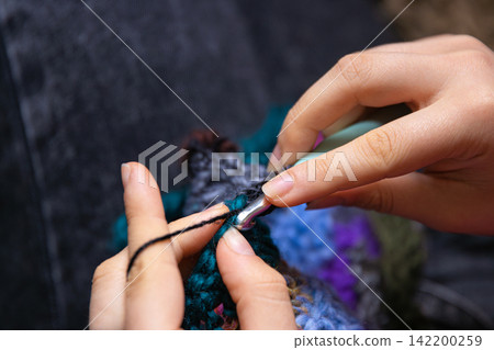 Closeup photo of young womans hands crocheting a colorful scarf using a crochet hook and vibrant yarn. Closeup photo of young womans hands crocheting a colorful scarf using a crochet hook and vibrant yarn. 142200259