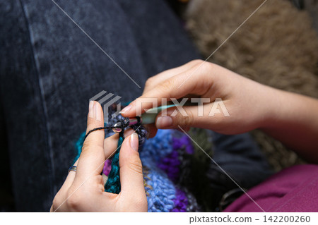 Closeup photo of young womans hands crocheting a colorful scarf using a crochet hook and vibrant yarn. Closeup photo of young womans hands crocheting a colorful scarf using a crochet hook and vibrant yarn. 142200260