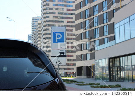 The car stopped in front of a parking sign for drivers with disabilities allowing them to park on the sidewalk. Rules of car parking in modern city The car stopped in front of a parking sign for drivers with disabilities allowing them to park on the sidewalk. Rules of car parking in modern city 142200514