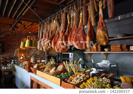Jamon and cured sausages above the restaurant counter with spices and traditional bread on it. Traditional dry meat. Hamon and cured meat Jamon and cured sausages above the restaurant counter with spices and traditional bread on it. Traditional dry meat. Hamon and cured meat 142200557