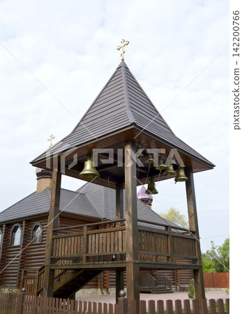wooden tower with church bells and a cross on the background of the church wooden tower with church bells and a cross on the background of the church 142200766