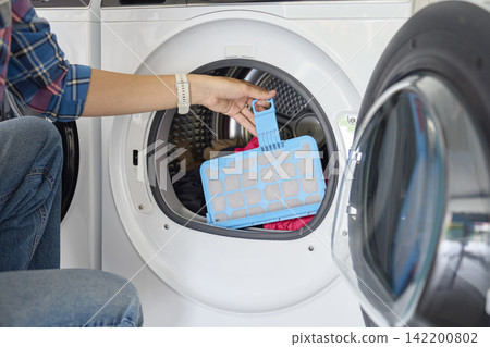 Woman removes lint filter from open tumble dryer with clothes inside 142200802