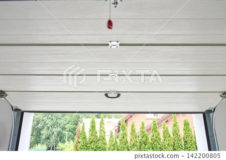 Sectional garage door is partially open with a view outside from inside the garage Sectional garage door is partially open with a view outside from inside the garage 142200805