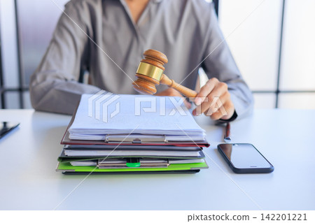 Attorney holding a wooden gavel above a pile of court paperwork on a workspace table. 142201221