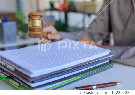 Attorney holding a wooden gavel above a pile of court paperwork on a workspace table. Attorney holding a wooden gavel above a pile of court paperwork on a workspace table. 142201223