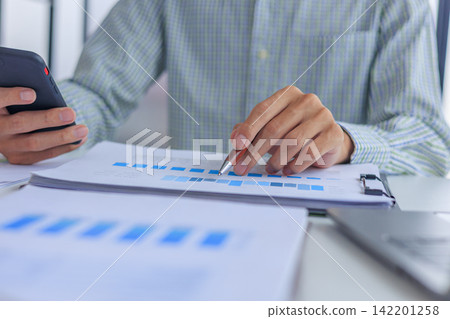 Professional financial analyst working on analyzing charts and documents using smartphone in modern office. Professional financial analyst working on analyzing charts and documents using smartphone in modern office. 142201258