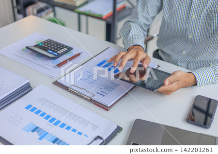 Businessman working in office using tablet while reviewing and analyzing graph data at desk. Businessman working in office using tablet while reviewing and analyzing graph data at desk. 142201261