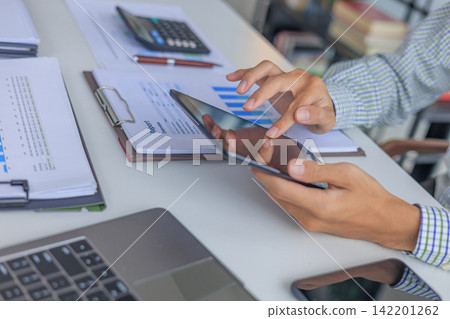 Professional financial analyst using tablet while working on analyzing charts and documents in modern office. Professional financial analyst using tablet while working on analyzing charts and documents in modern office. 142201262