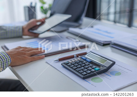 Professional financial analyst using tablet while working on analyzing charts and documents in modern office. Professional financial analyst using tablet while working on analyzing charts and documents in modern office. 142201263