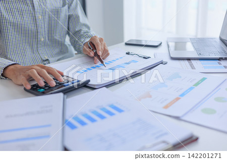 Businessman working at office desk using calculator analyzing financial charts data in office. Businessman working at office desk using calculator analyzing financial charts data in office. 142201271