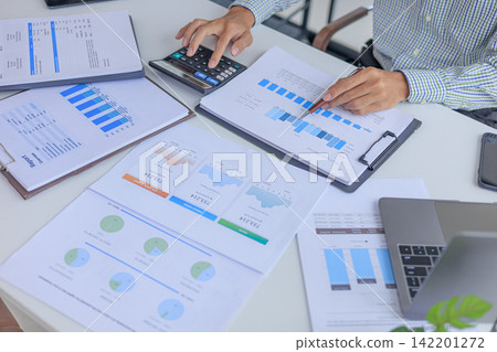 Businessman working at office desk using calculator analyzing financial charts data in office. Businessman working at office desk using calculator analyzing financial charts data in office. 142201272