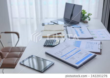 Modern white office workspace of financial or accounting tasks, featuring a laptop, a tablet, financial charts, reports, a calculator, and a notebook on a white desk. Modern white office workspace of financial or accounting tasks, featuring a laptop, a tablet, financial charts, reports, a calculator, and a notebook on a white desk. 142201276