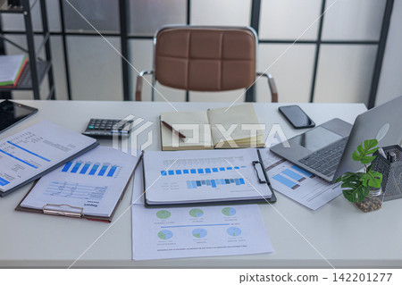 Modern white office workspace of financial or accounting tasks, featuring a laptop, a tablet, financial charts, reports, a calculator, and a notebook on a white desk. Modern white office workspace of financial or accounting tasks, featuring a laptop, a tablet, financial charts, reports, a calculator, and a notebook on a white desk. 142201277