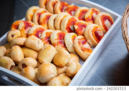 Tray of assorted baked bread rolls with tomato sauce and melted cheese on metal surface, showing golden crusts, soft texture, and fresh bakery presentation for food service use 142201513