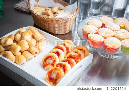Assorted fresh baked pastries, bread rolls, fruit filled rounds, sugar dusted muffins arranged on serving trays with wicker basket for breakfast buffet or catering display Assorted fresh baked pastries, bread rolls, fruit filled rounds, sugar dusted muffins arranged on serving trays with wicker basket for breakfast buffet or catering display 142201514