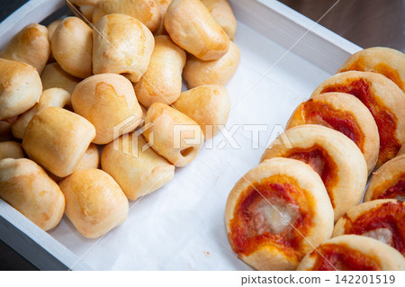 mini pizza rolls baked and arranged on a tray in a kitchen setting with golden brown and red colors and parchment paper background, delicious and appetizing top-down view. 142201519
