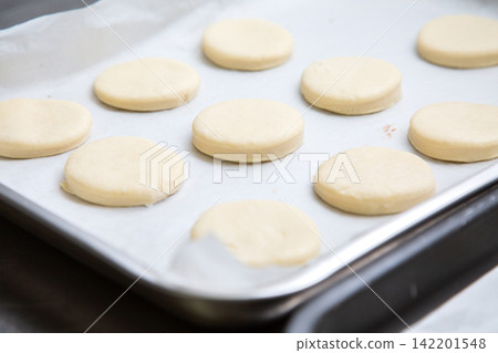 Rows of pale round cookie dough portions on parchment lined baking tray, ready for oven baking in bright kitchen light with soft shallow focus and clean minimal food preparation scene Rows of pale round cookie dough portions on parchment lined baking tray, ready for oven baking in bright kitchen light with soft shallow focus and clean minimal food preparation scene 142201548