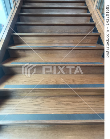 Wooden staircase with blue safety strips leading upward indoors Wooden staircase with blue safety strips leading upward indoors 142201685