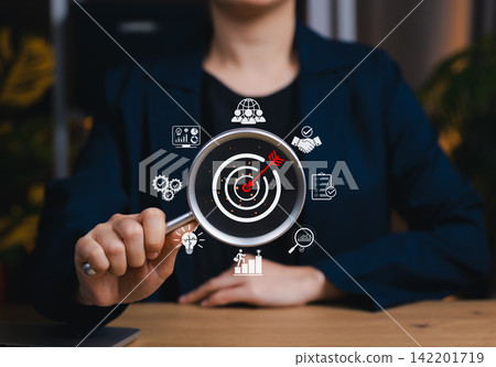 Business goals and target achievement concept. Magnifying glass focused on target with marketing and business strategy icon, goal setting, strategic planning, market research, performance optimization 142201719
