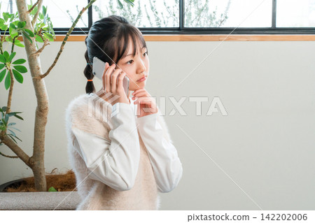 Elementary school and junior high school girls sitting on the sofa at home talking on their smartphones Elementary school and junior high school girls sitting on the sofa at home talking on their smartphones 142202006