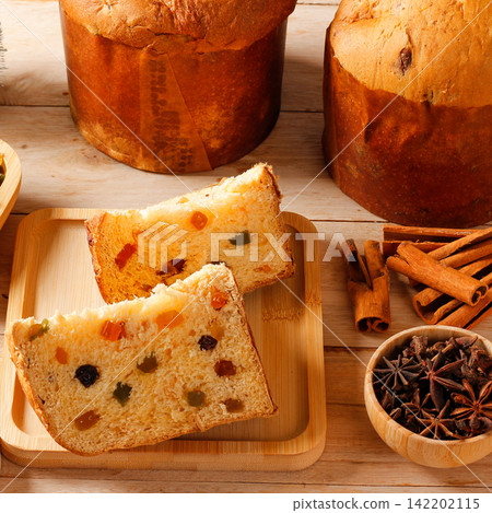 Slices of Christmas panettone with candied fruit, accompanied by dried orange, cinnamon, and star anise on a rustic table Slices of Christmas panettone with candied fruit, accompanied by dried orange, cinnamon, and star anise on a rustic table 142202115