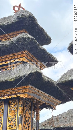 Balinese Meru tower featuring traditional thatched roofs and intricate golden carvings against a bright sky, symbolizing spiritual heritage and religious architecture in Bali, Indonesia Balinese Meru tower featuring traditional thatched roofs and intricate golden carvings against a bright sky, symbolizing spiritual heritage and religious architecture in Bali, Indonesia 142202381
