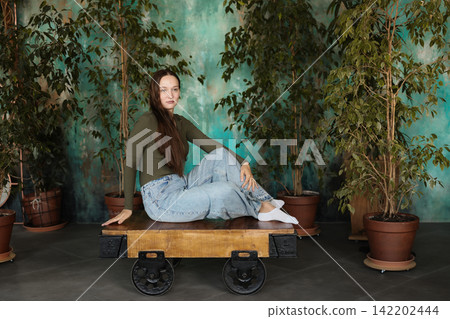 Relaxed young woman sitting among potted plants in studio environment 142202444
