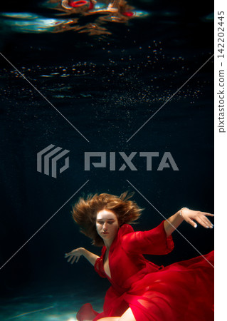 Tranquil female figure in crimson attire gliding beneath water effortlessly 142202445