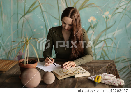 Woman writing quietly. Woman engaged in journal writing at cozy desk Woman writing quietly. Woman engaged in journal writing at cozy desk 142202497