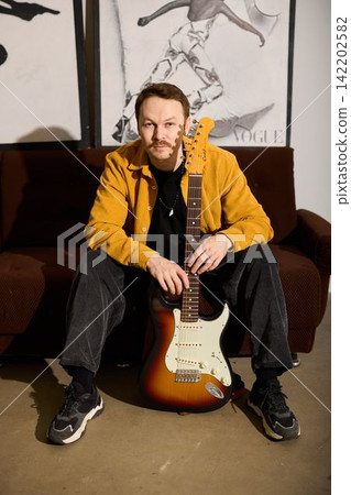 Session musician seated with electric guitar, relaxed studio portrait Session musician seated with electric guitar, relaxed studio portrait 142202582