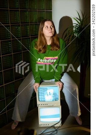 Woman leaning on old computer with vibrant studio setting behind her Woman leaning on old computer with vibrant studio setting behind her 142202589