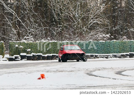 Red vehicle swiftly avoids cones on icy track with skid marks visible Red vehicle swiftly avoids cones on icy track with skid marks visible 142202653