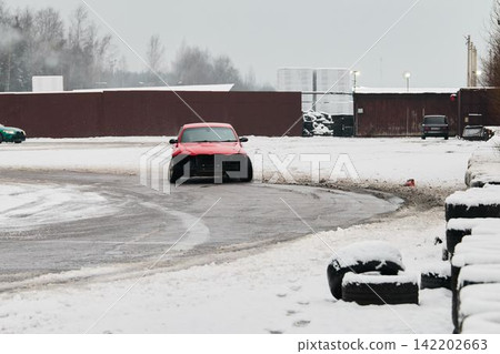 Red car moves closer to camera over wintry snowy pathway with muted shades Red car moves closer to camera over wintry snowy pathway with muted shades 142202663
