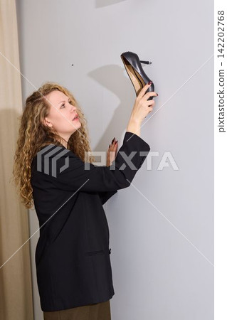 Woman examines shoe. Woman with curly hair scrutinizes shoe features Woman examines shoe. Woman with curly hair scrutinizes shoe features 142202768