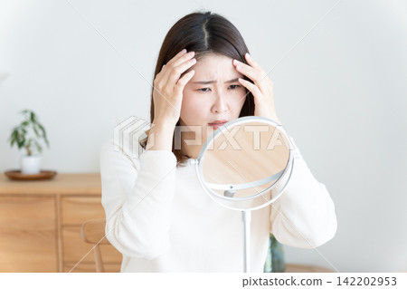一位女士對著鏡子檢查自己的髮際線。 142202953